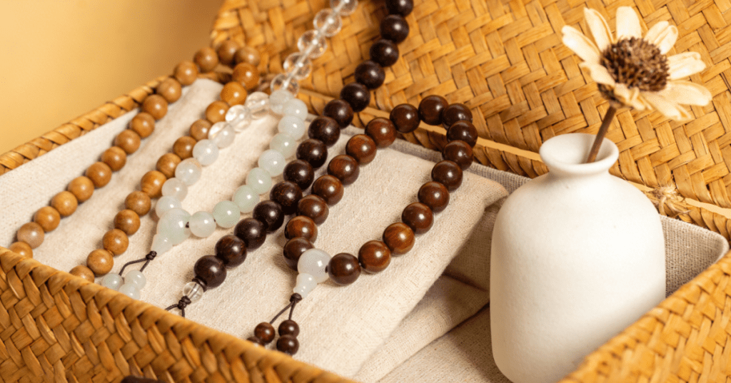 Multiple malas of different materials displayed in a Japanese-style bamboo storage box with a minimalist ceramic flower vase